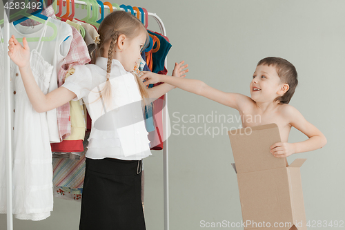 Image of Two little children standing near a hanger with clothes at home 