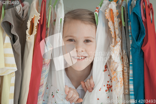 Image of portrait of a little girl standing near a hanger with clothes