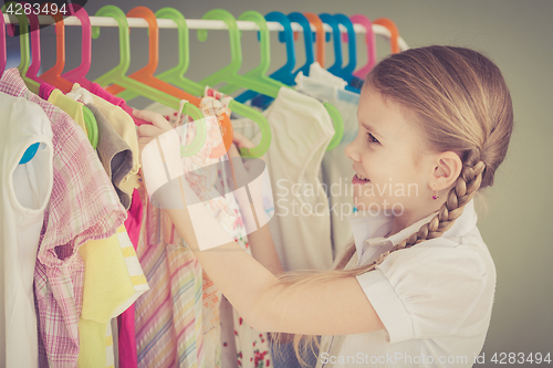 Image of portrait of a little girl standing near a hanger with clothes