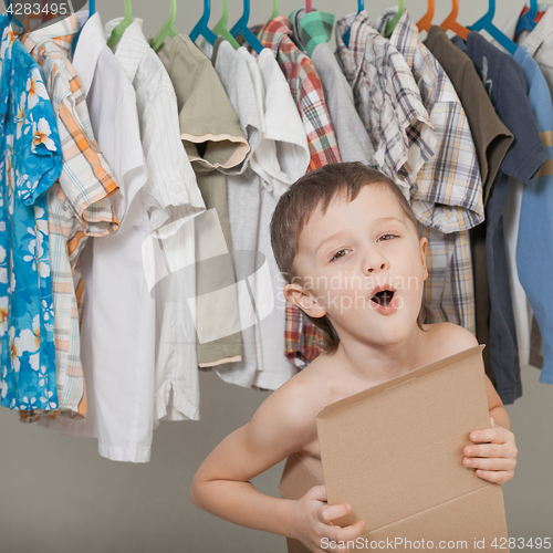 Image of portrait of a little boy standing near a hanger with clothes