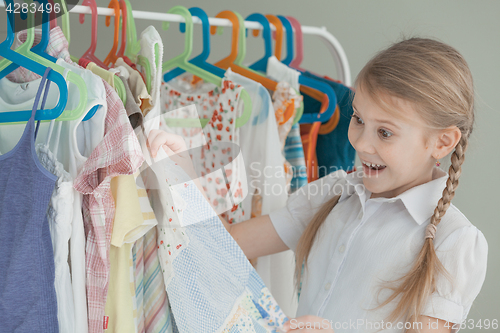 Image of portrait of a little girl standing near a hanger with clothes
