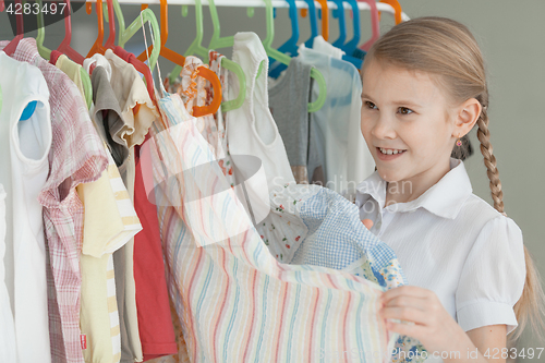 Image of portrait of a little girl standing near a hanger with clothes