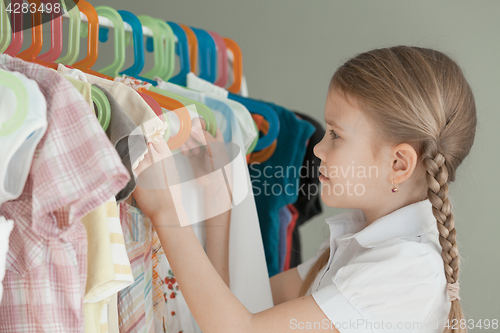 Image of portrait of a little girl standing near a hanger with clothes