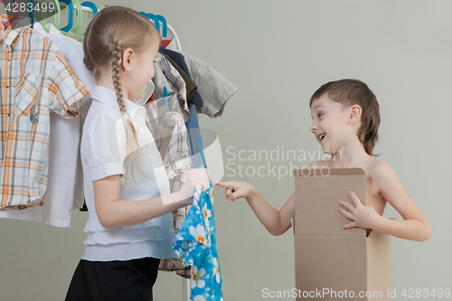 Image of Two little children standing near a hanger with clothes at home 