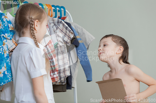 Image of Two little children standing near a hanger with clothes at home 