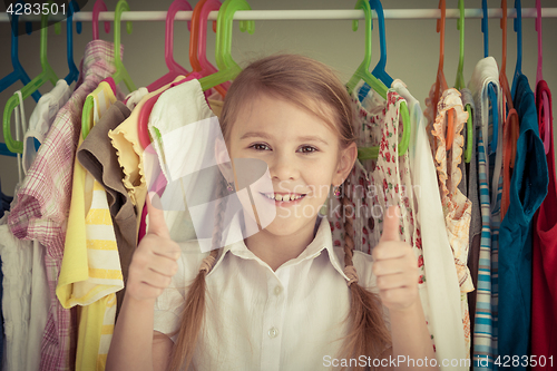 Image of portrait of a little girl standing near a hanger with clothes