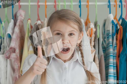 Image of portrait of a little girl standing near a hanger with clothes