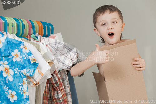 Image of portrait of a little boy standing near a hanger with clothes