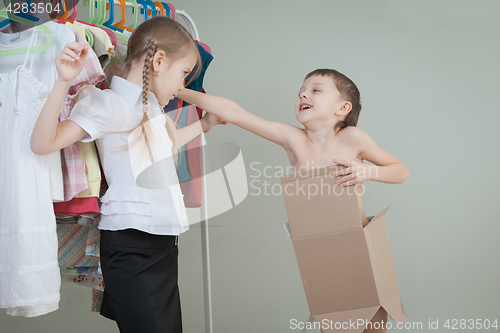 Image of Two little children standing near a hanger with clothes at home 