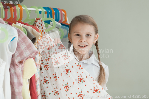 Image of portrait of a little girl standing near a hanger with clothes