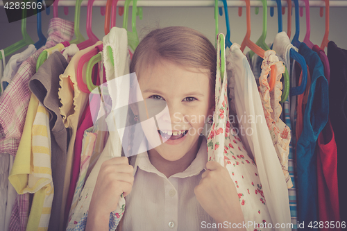 Image of portrait of a little girl standing near a hanger with clothes