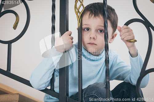 Image of one sad little boy sitting on the stairs in house at the day tim