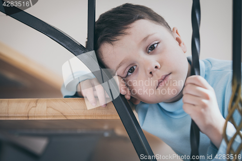 Image of one sad little boy sitting on the stairs in house at the day tim