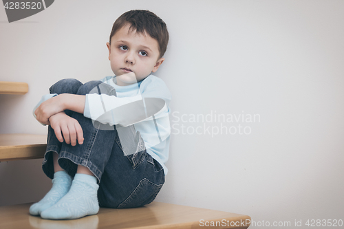 Image of one sad little boy sitting on the stairs in house at the day tim