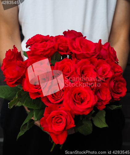 Image of Male person holding a beautiful bouquet of red roses wearing whi