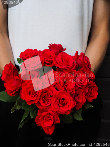 Image of Male person holding a beautiful bouquet of red roses wearing whi