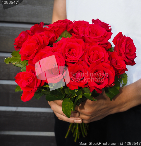 Image of Male person holding a beautiful bouquet of red roses wearing whi