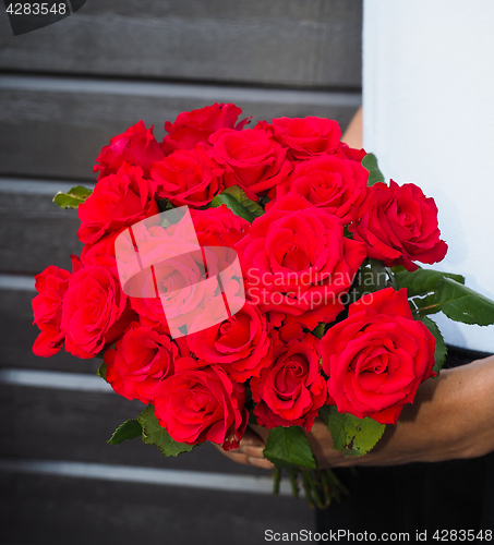 Image of Male person holding a beautiful bouquet of red roses wearing whi