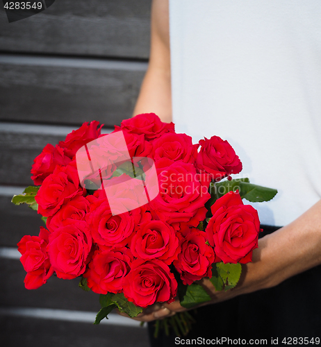 Image of Male person holding a beautiful bouquet of red roses wearing whi