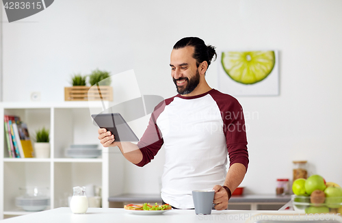 Image of man with tablet pc eating at home kitchen