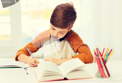 Image of student boy with book writing to notebook at home