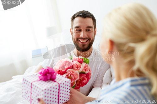 Image of happy couple with gift box in bed at home