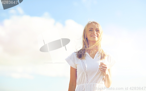 Image of smiling young woman in white dress over blue sky