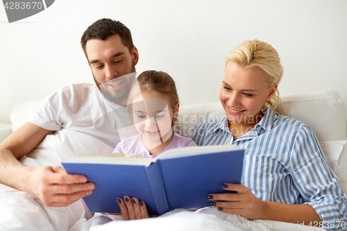 Image of happy family reading book in bed at home