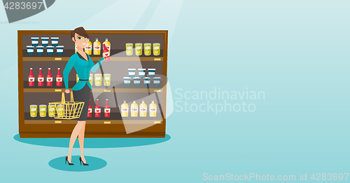 Image of Woman holding shopping basket and bottle of sauce.