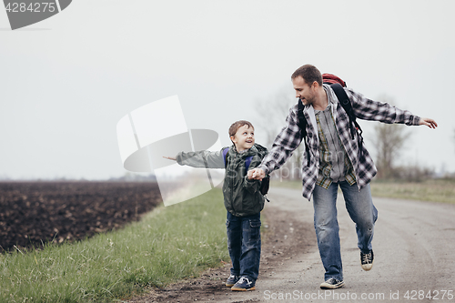 Image of Father and son walking on the road at the day time.