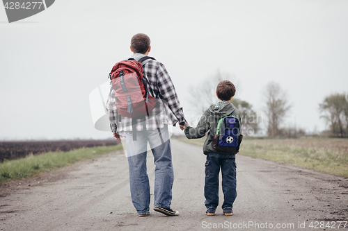 Image of Father and son walking on the road at the day time.