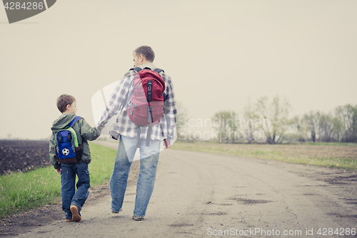 Image of Father and son walking on the road at the day time.