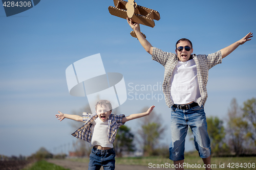 Image of Father and son playing with cardboard toy airplane in the park a