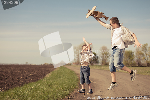 Image of Father and son playing with cardboard toy airplane in the park a