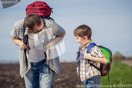 Image of Father and son walking on the road at the day time.