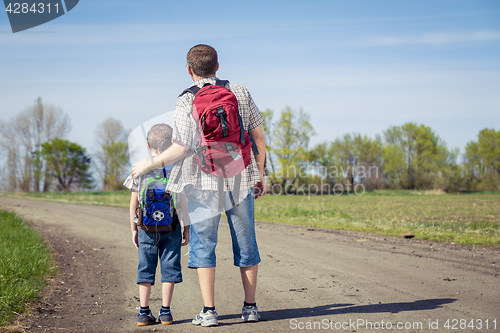 Image of Father and son walking on the road at the day time.