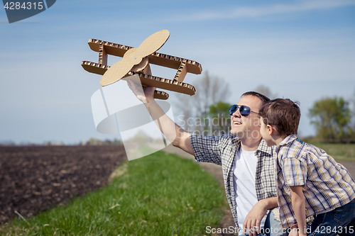 Image of Father and son playing with cardboard toy airplane in the park a