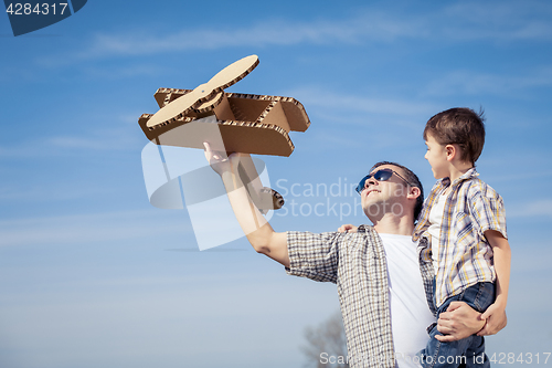 Image of Father and son playing with cardboard toy airplane in the park a