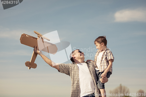 Image of Father and son playing with cardboard toy airplane in the park a