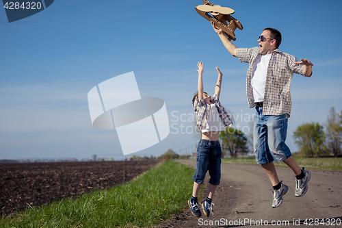 Image of Father and son playing with cardboard toy airplane in the park a