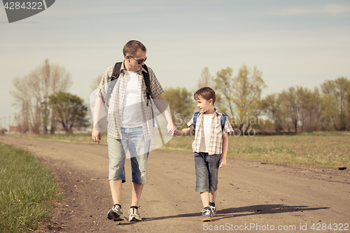 Image of Father and son walking on the road at the day time.