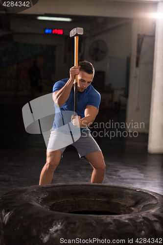 Image of man workout with hammer and tractor tire