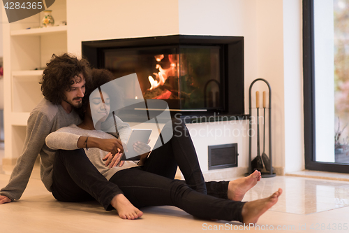 Image of multiethnic couple using tablet computer on the floor