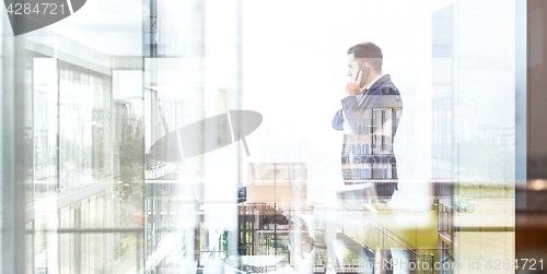 Image of Businessman talking on a mobile phone while looking through window.