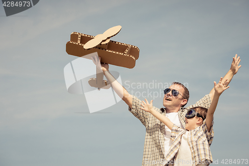 Image of Father and son playing with cardboard toy airplane in the park a