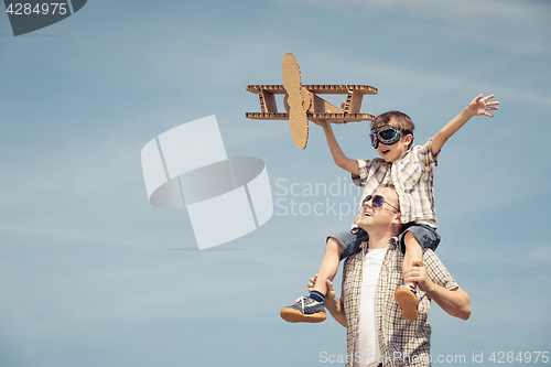 Image of Father and son playing with cardboard toy airplane in the park a