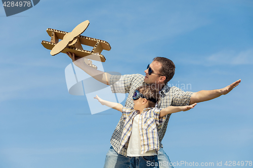 Image of Father and son playing with cardboard toy airplane in the park a