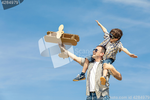 Image of Father and son playing with cardboard toy airplane in the park a