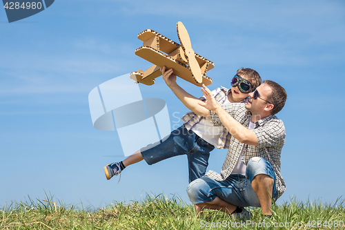 Image of Father and son playing with cardboard toy airplane in the park a