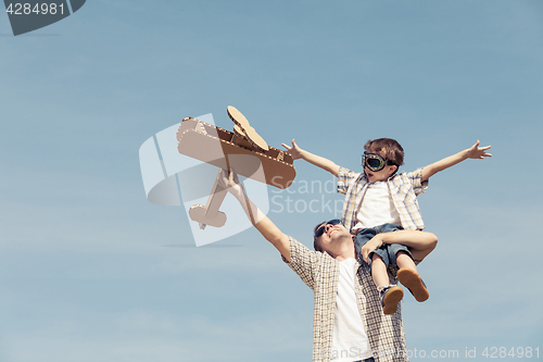 Image of Father and son playing with cardboard toy airplane in the park a